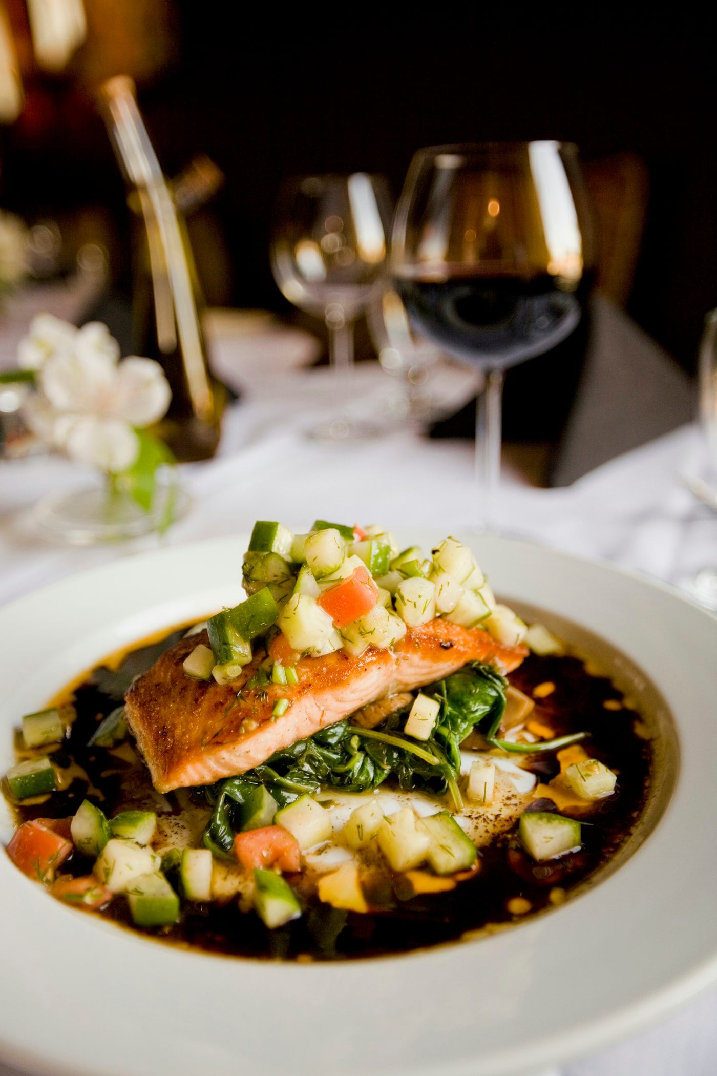 Seared salmon plated with herbs, cucumber, and a dark sauce